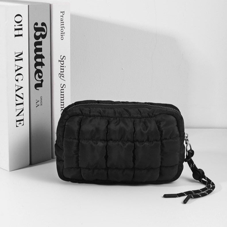 Black quilted pouch with a strap next to a magazine on a white background
