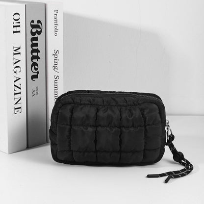 Black quilted pouch with a strap next to a magazine on a white background